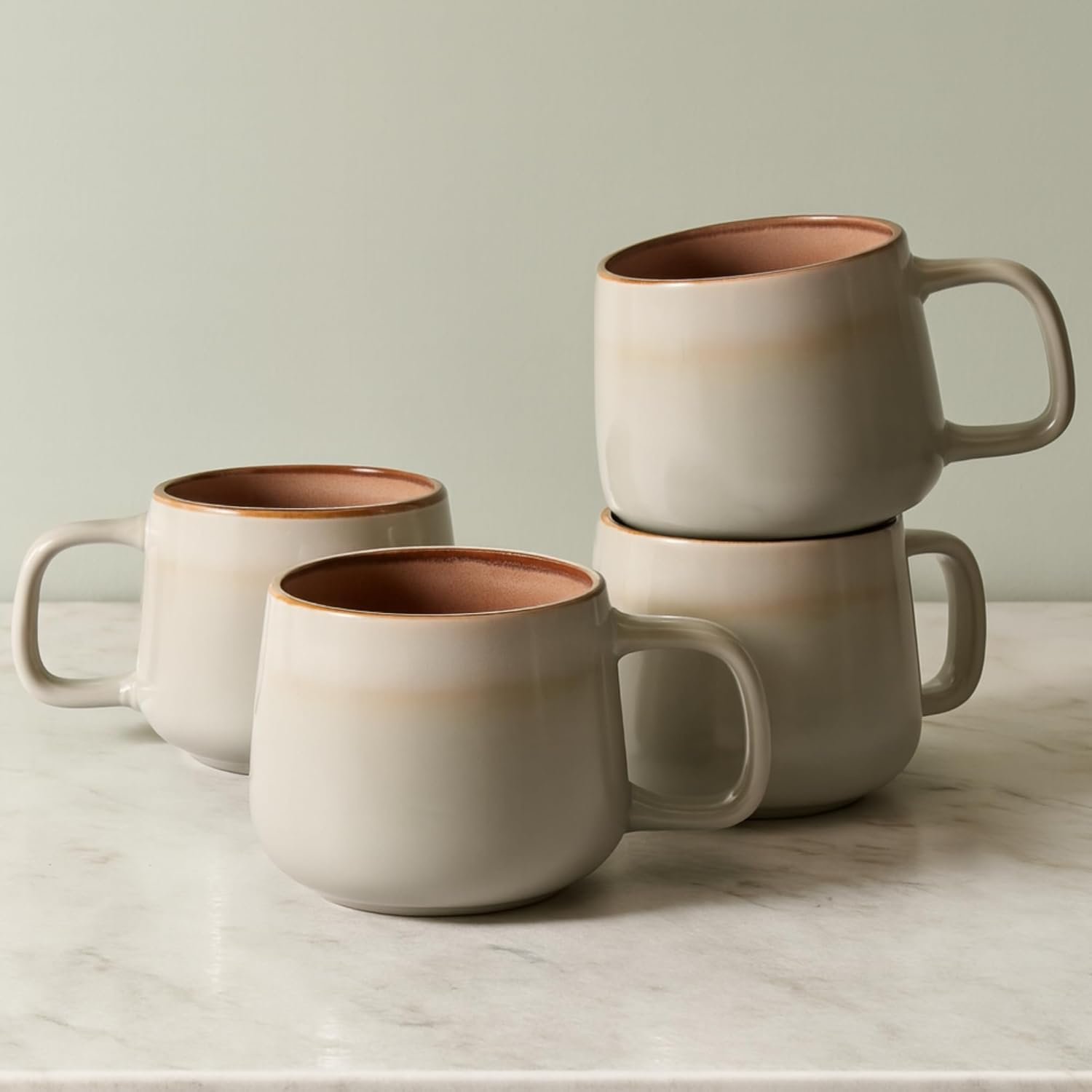 Sage ash ceramic coffee mug set of four with warm brown interior styled on a neutral kitchen counter